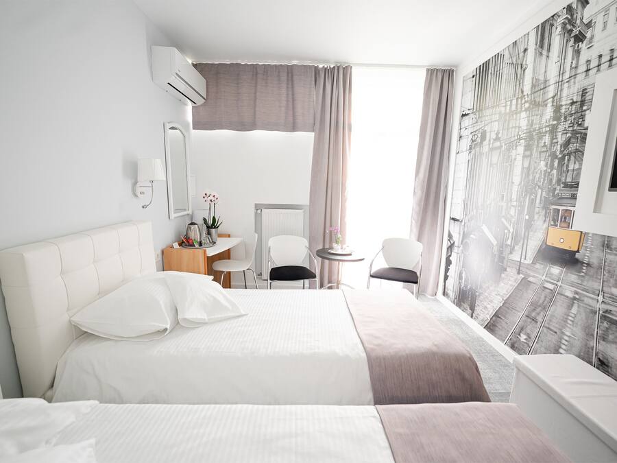 A hotel room with a large bed, a desk, a chair, a small table with a lamp, and a wall-mounted TV.