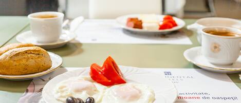 En morgenmadsopstilling med æg, tomater og brød på en tallerken, samt kaffekopper på et bord.