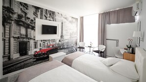 A hotel room with a large bed, a TV mounted on the wall, a small table with a lamp, and a mural of a city street. - MyContinental Suceava (Suceava)