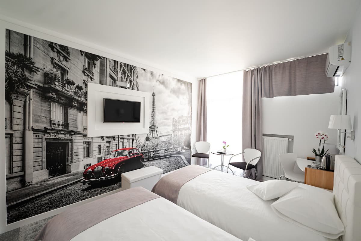 A hotel room with a large bed, a TV mounted on the wall, a small table with a lamp, and a mural of a city street.