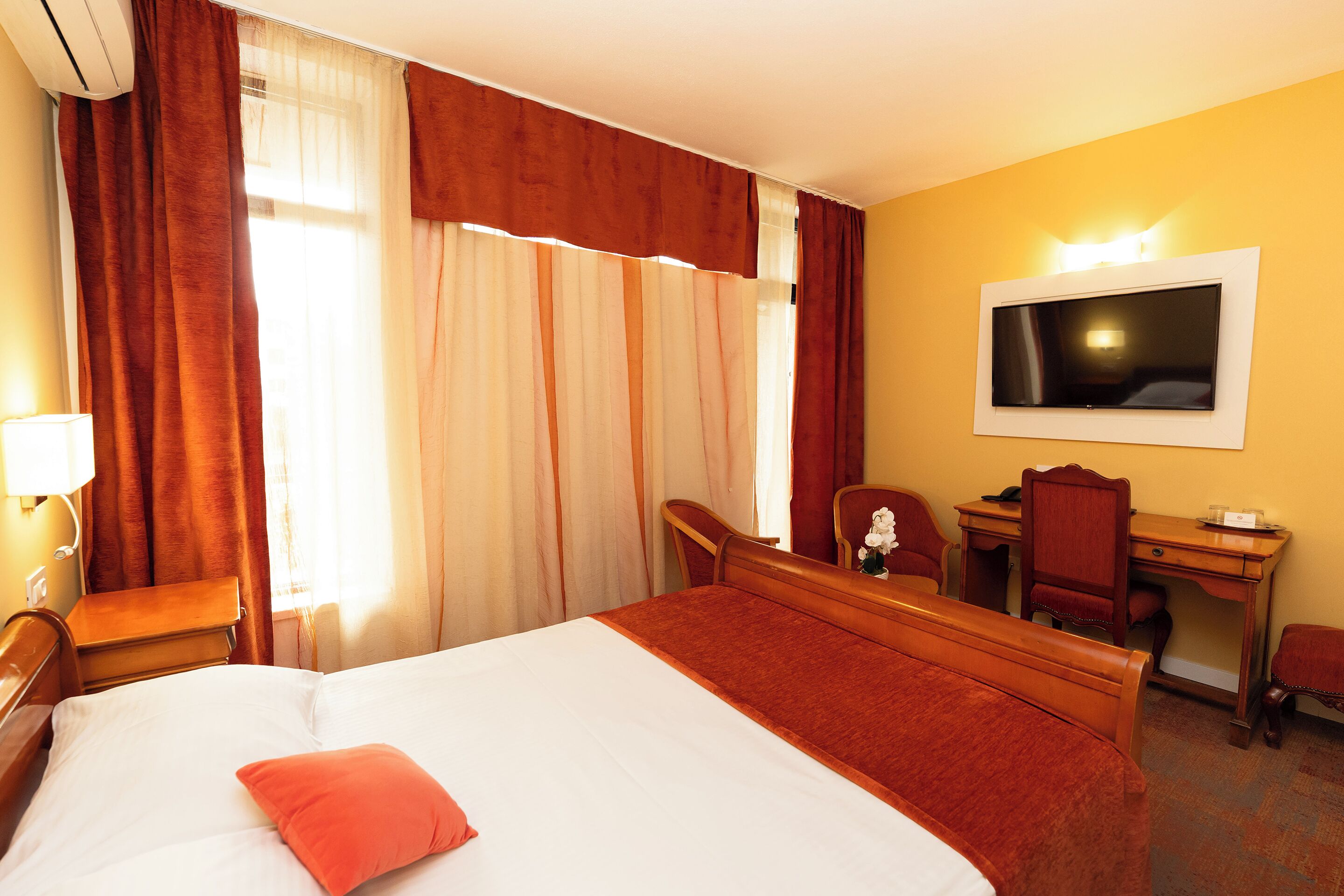 A hotel room with a large bed, a desk, a chair, a TV, and curtains.
