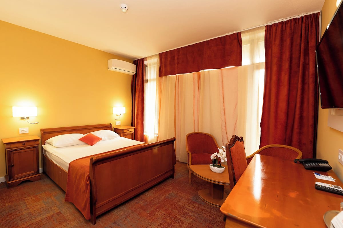 A hotel room with a bed, bedside tables, a desk, and a chair.