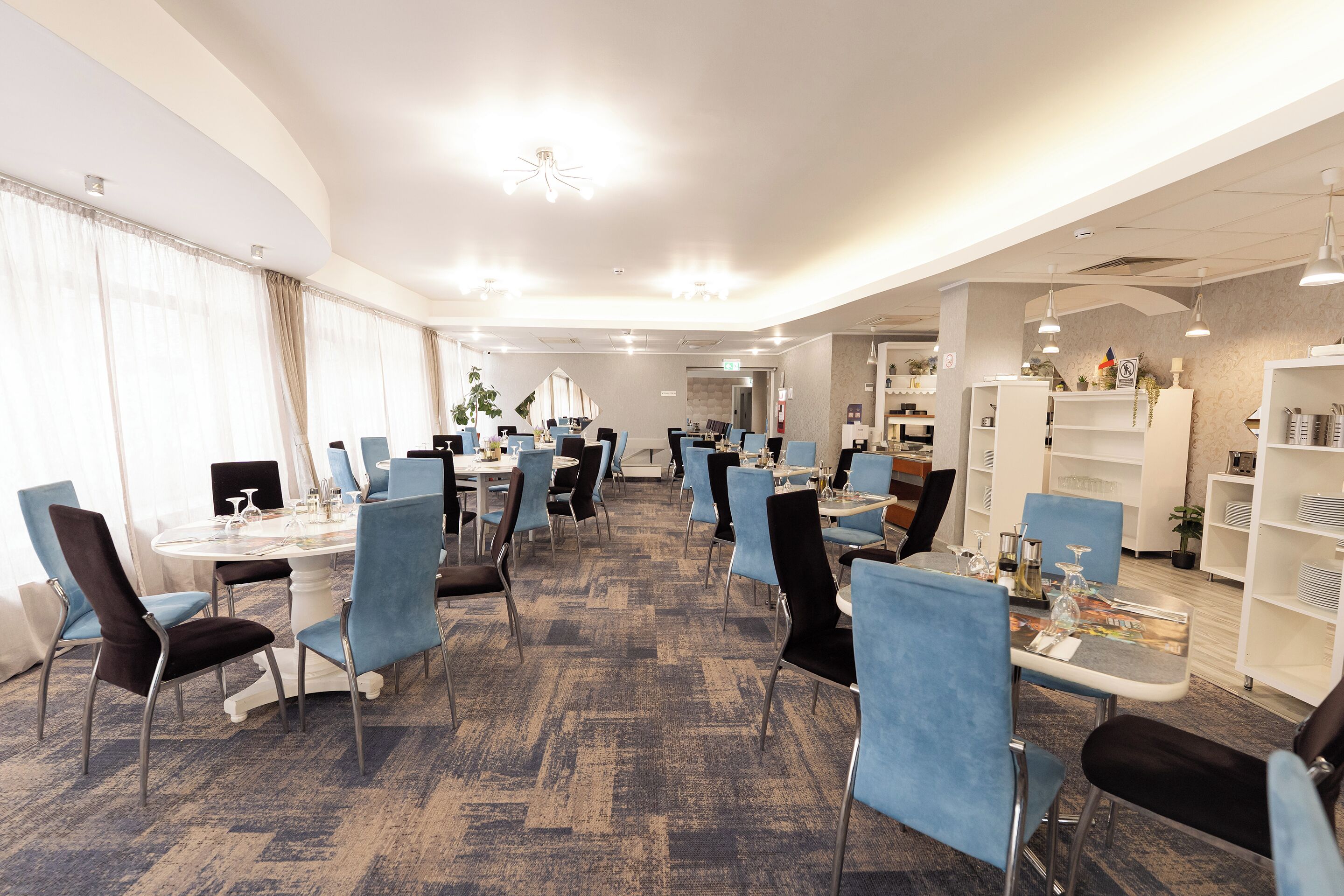 A hotel dining area with round tables, blue chairs, and a carpeted floor.