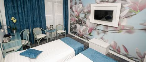 A hotel room with two beds, a TV, a desk with a chair, and a wall with a floral mural.