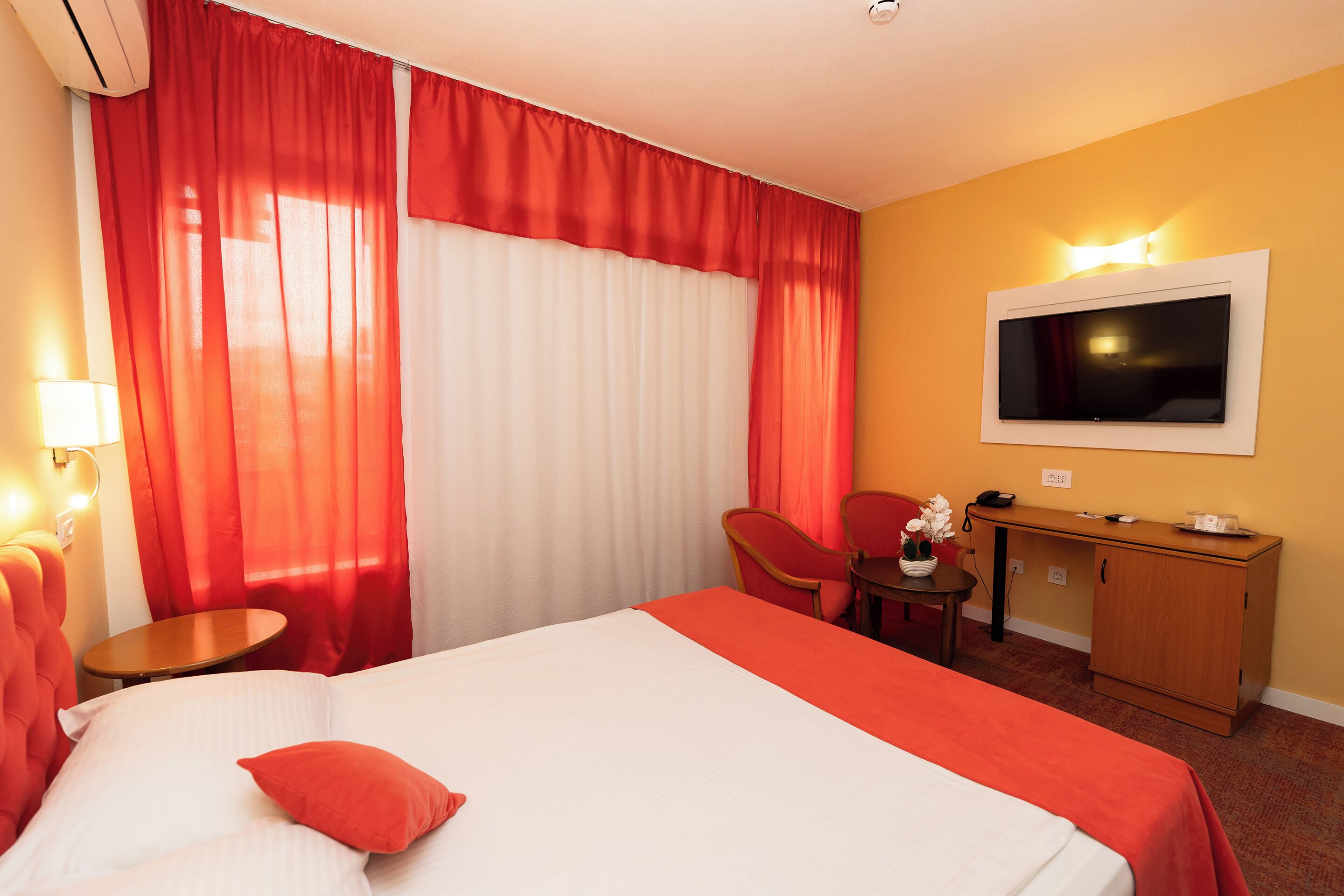 A hotel room with a bed, a desk, a chair, a TV, and a lamp.