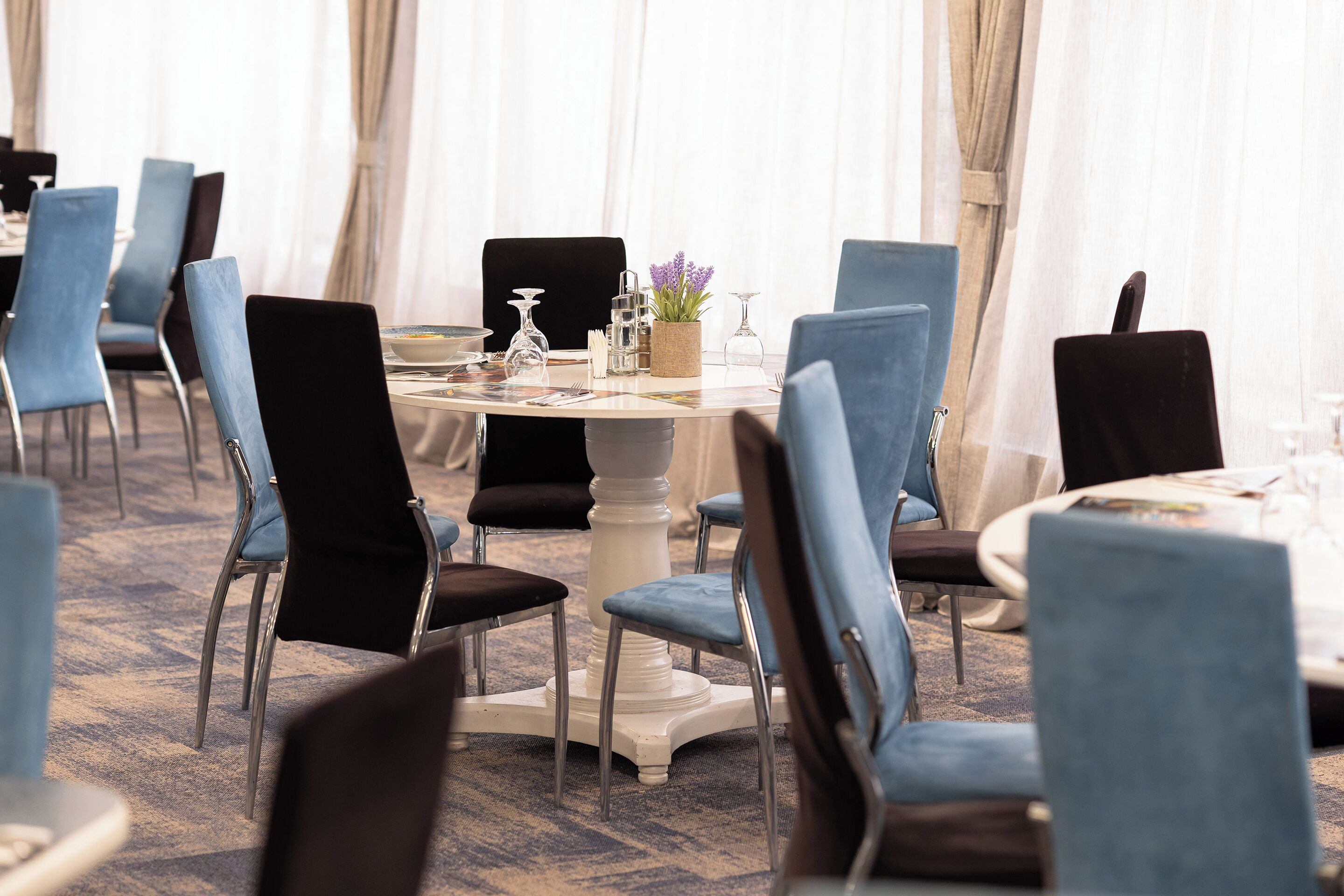 A dining area with round tables, blue and black upholstered chairs, and a carpeted floor.