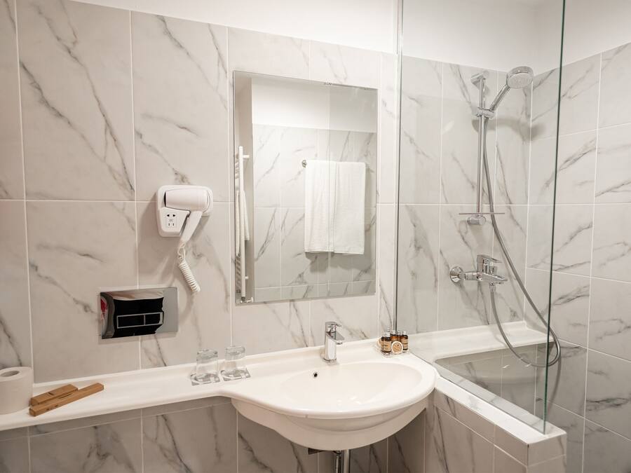 A bathroom with a white sink, a glass shower enclosure, a towel hanging on the wall, and a mirror.