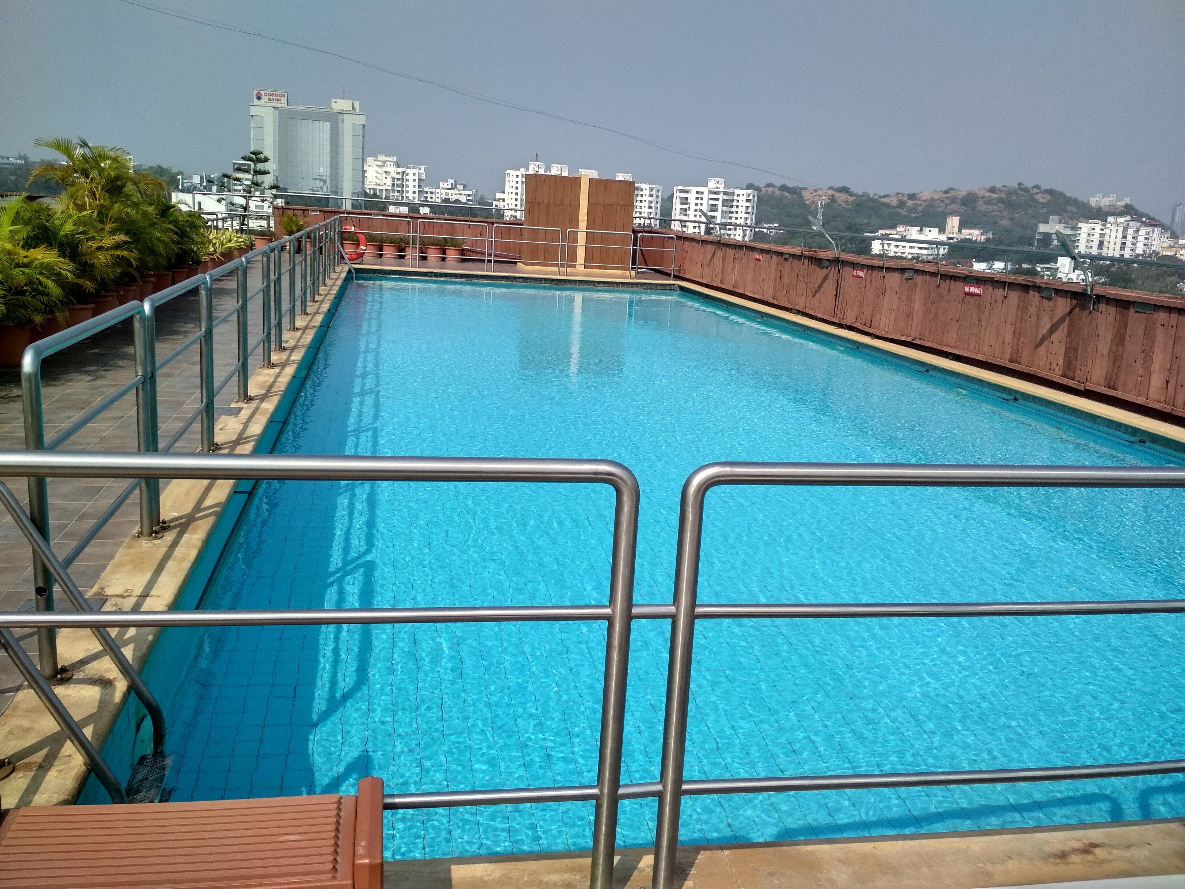 Piscina no terraço com grades de metal e vista para prédios da cidade ao fundo.