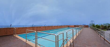 A rooftop pool with a wooden deck and metal railings.