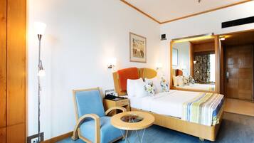 Ett hotellrum med en säng, en stol, ett litet bord, en golvlampa och en spegel.