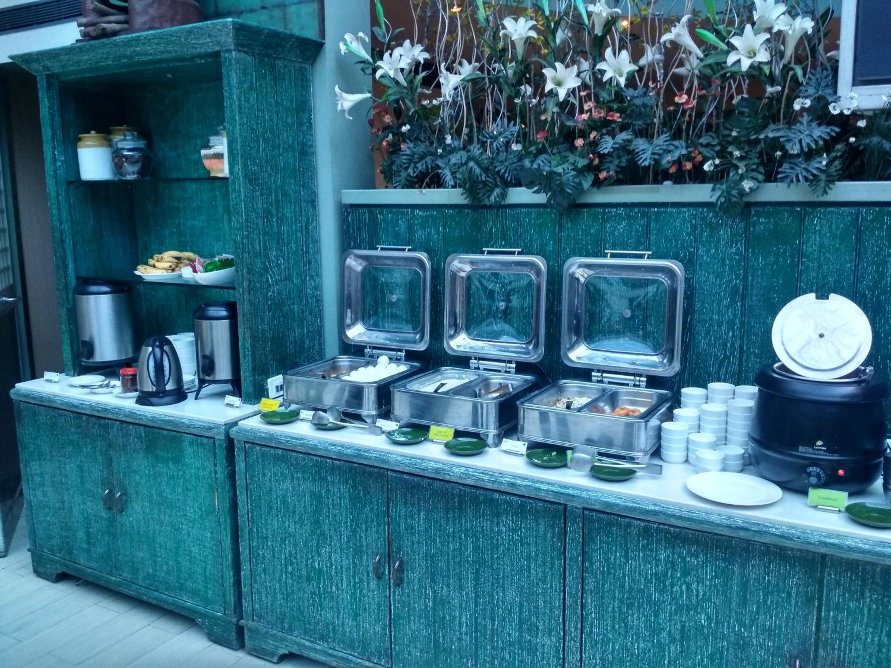A buffet setup with multiple food dispensers, a coffee machine, and a decorative plant arrangement.