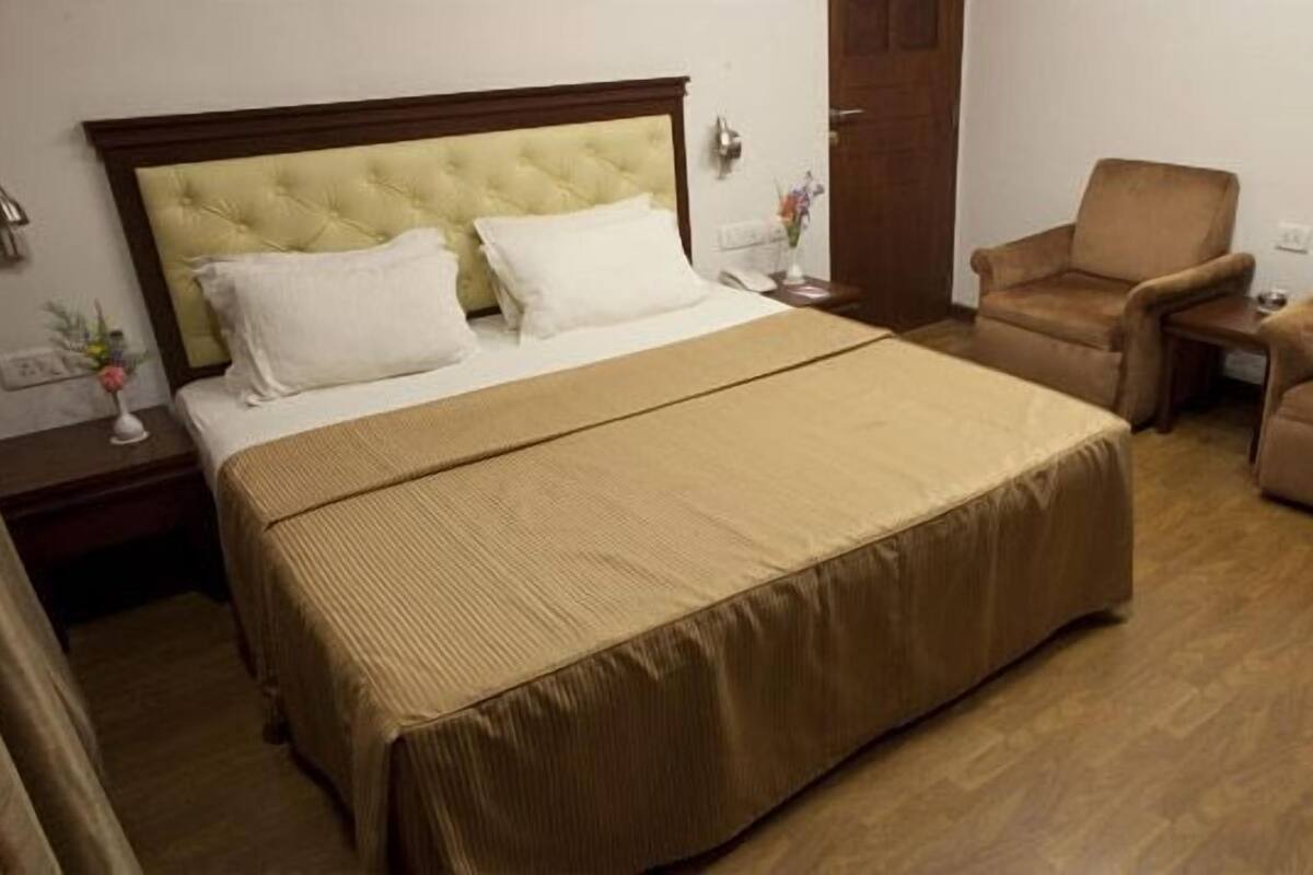 A hotel room with a large bed, two armchairs, a nightstand, and a wooden floor.