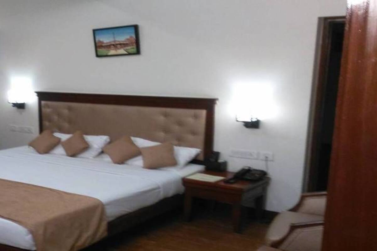 A hotel room with a large bed, a bedside table with a lamp, and a painting on the wall.