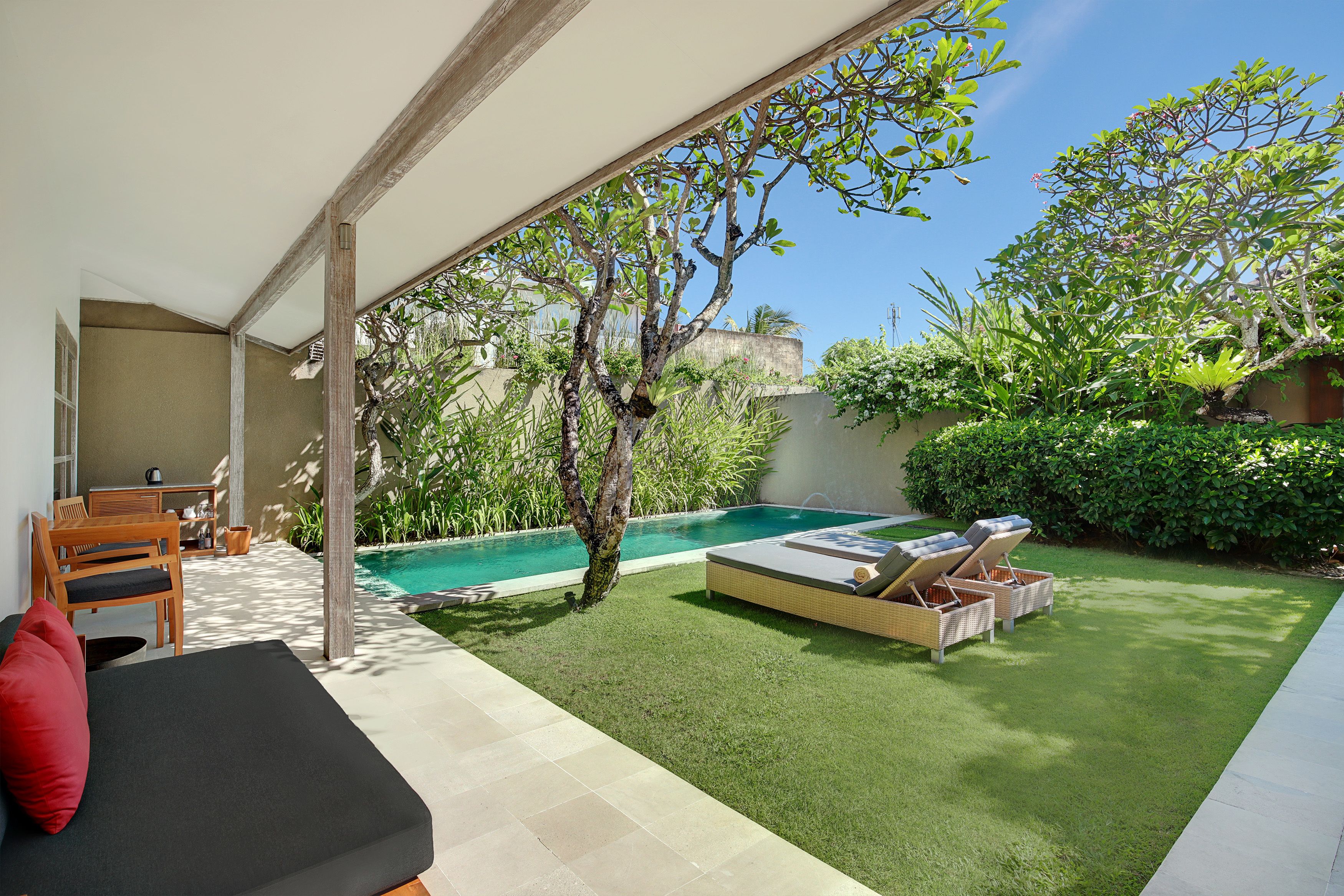 Un espacio exterior moderno con piscina, un área de estar techada y abundante vegetación.