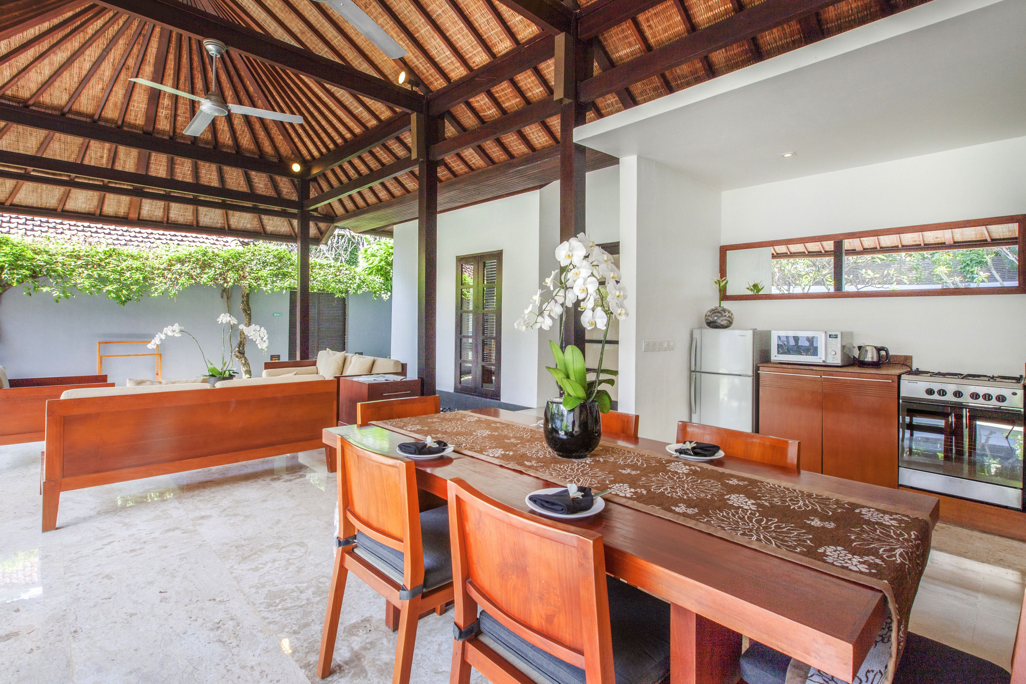 A dining area with a wooden table, chairs, and a ceiling fan. There is a kitchen area with a refrigerator and stove.