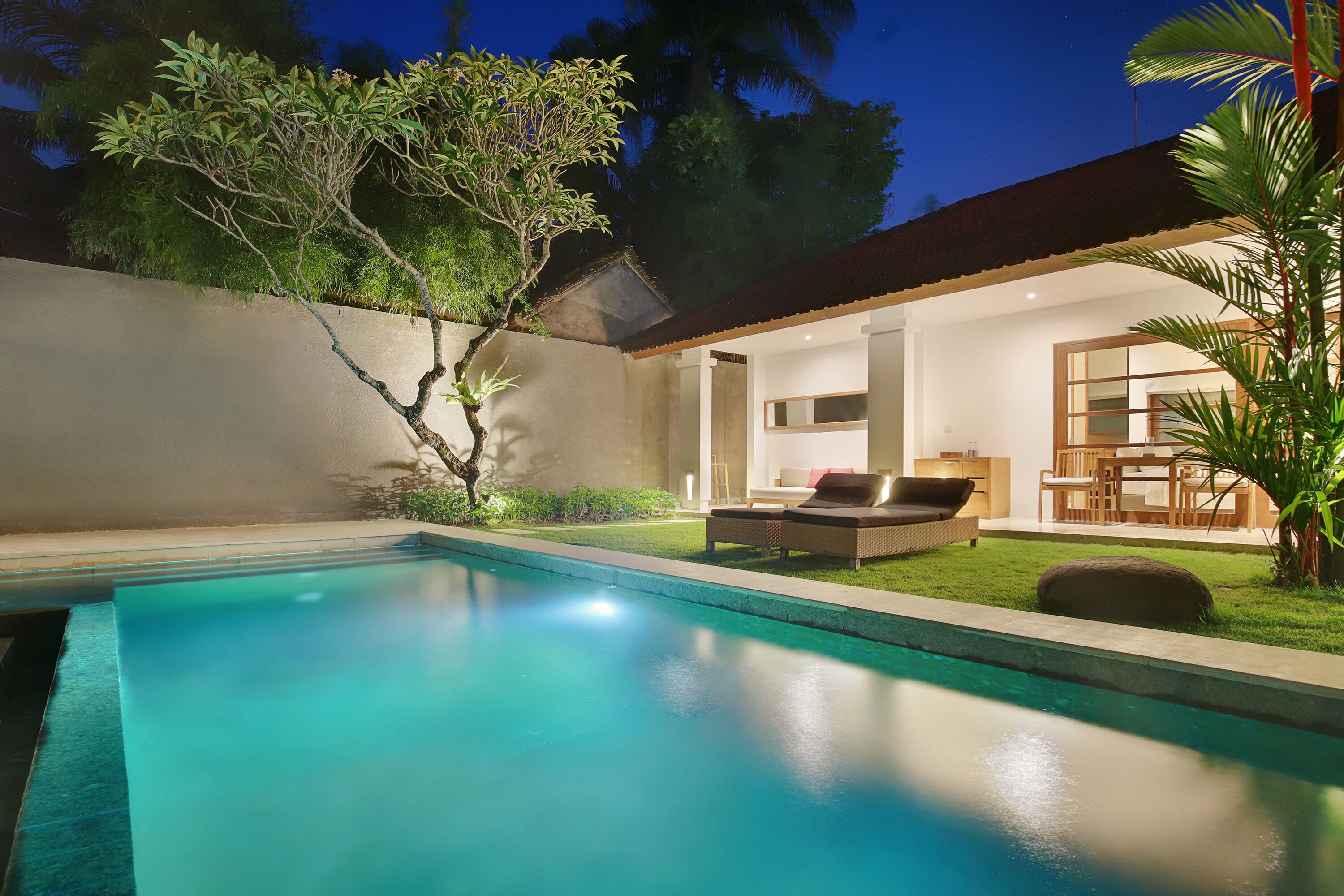 Una piscina con zona de patio, un conjunto de comedor y un espacio interior bien iluminado.