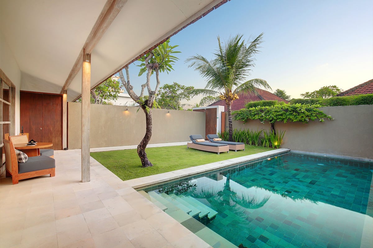 Een modern zwembadterras met een loungebed en een tafeltje, omgeven door een verzorgd gazon en een palmboom.