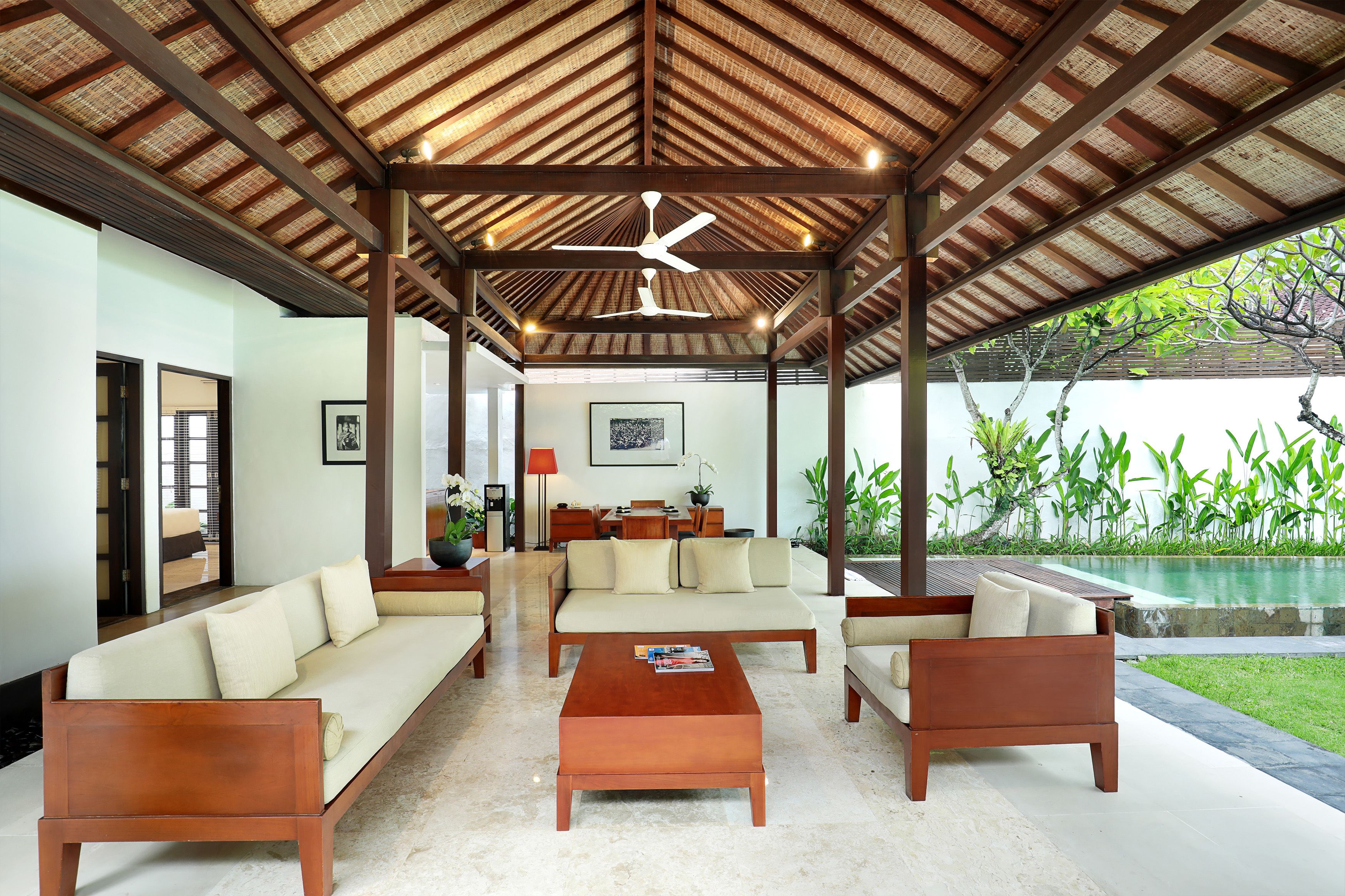 Una sala de estar moderna con techo alto, muebles de madera y vista a una piscina.