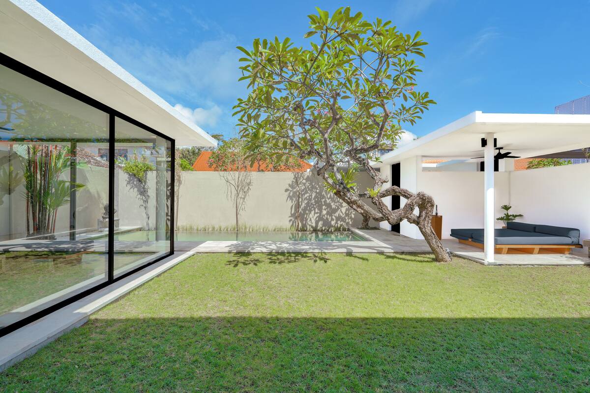 Een modern huis met een serre, een boom en een zithoek met kussens.
