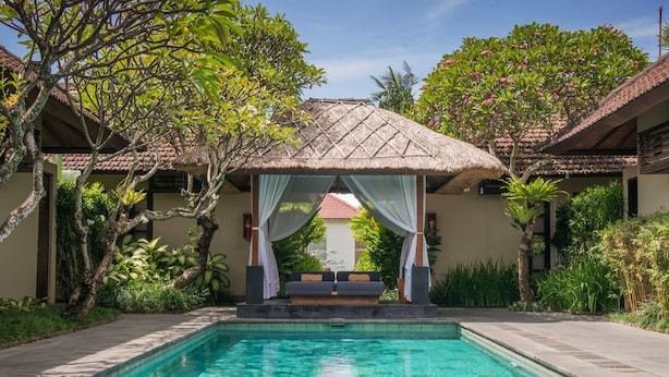 A clear swimming pool with a thatched-roof structure in the background. - Uma Sapna Seminyak (Seminyak)