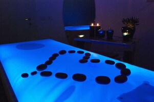 Una camilla de masaje con superficie iluminada en azul y una disposición de piedras en forma de corazón.