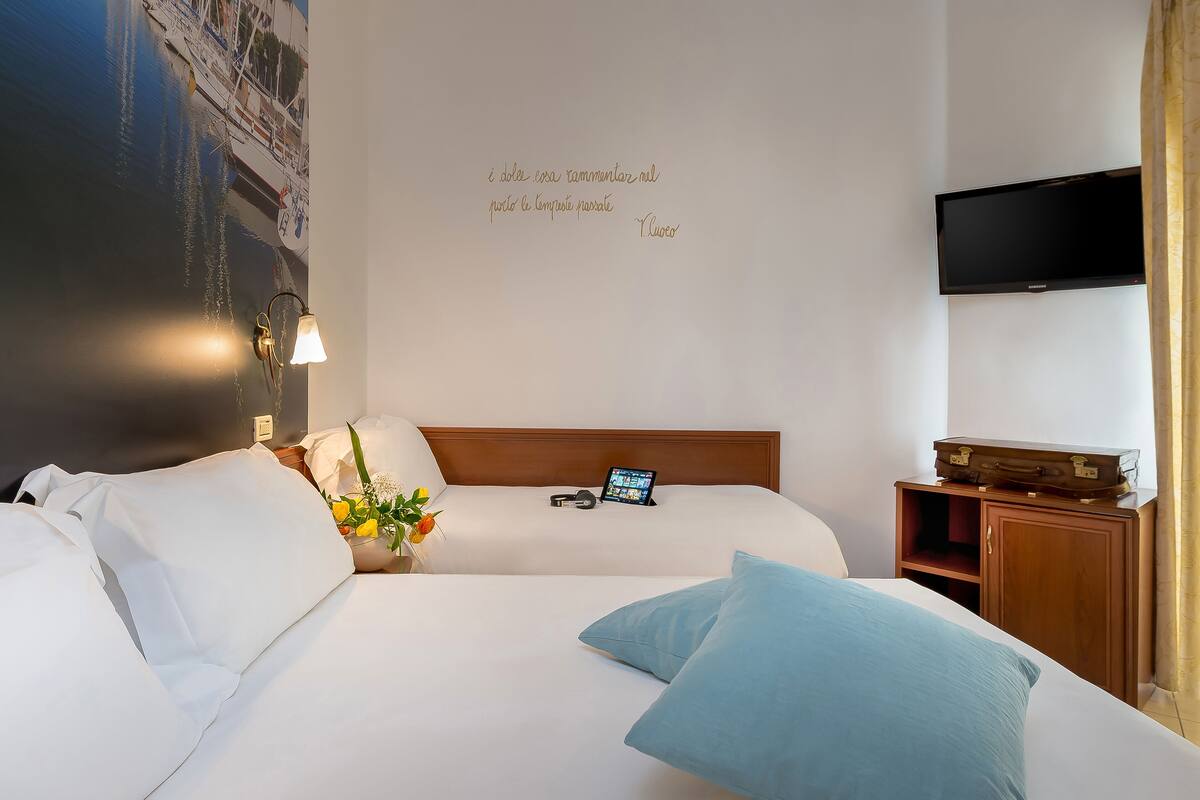 Habitación de hotel con dos camas, un televisor de pantalla plana montado en la pared y una cita decorando la pared.