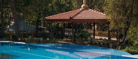Une piscine dotée d’un kiosque et entourée de verdure.