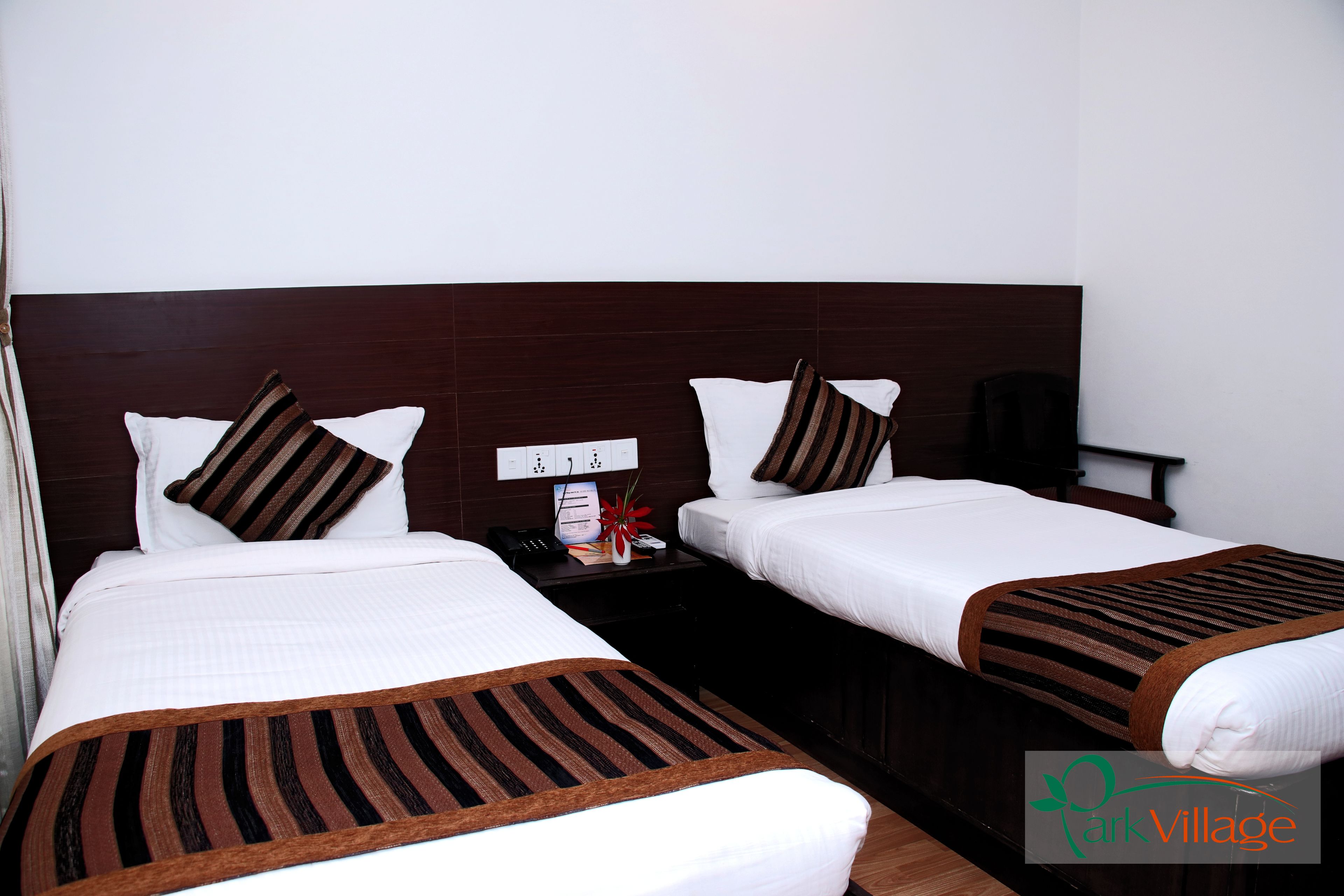 A hotel room with two beds, each with white bedding and striped blankets. There is a nightstand with a phone and a vase with flowers.