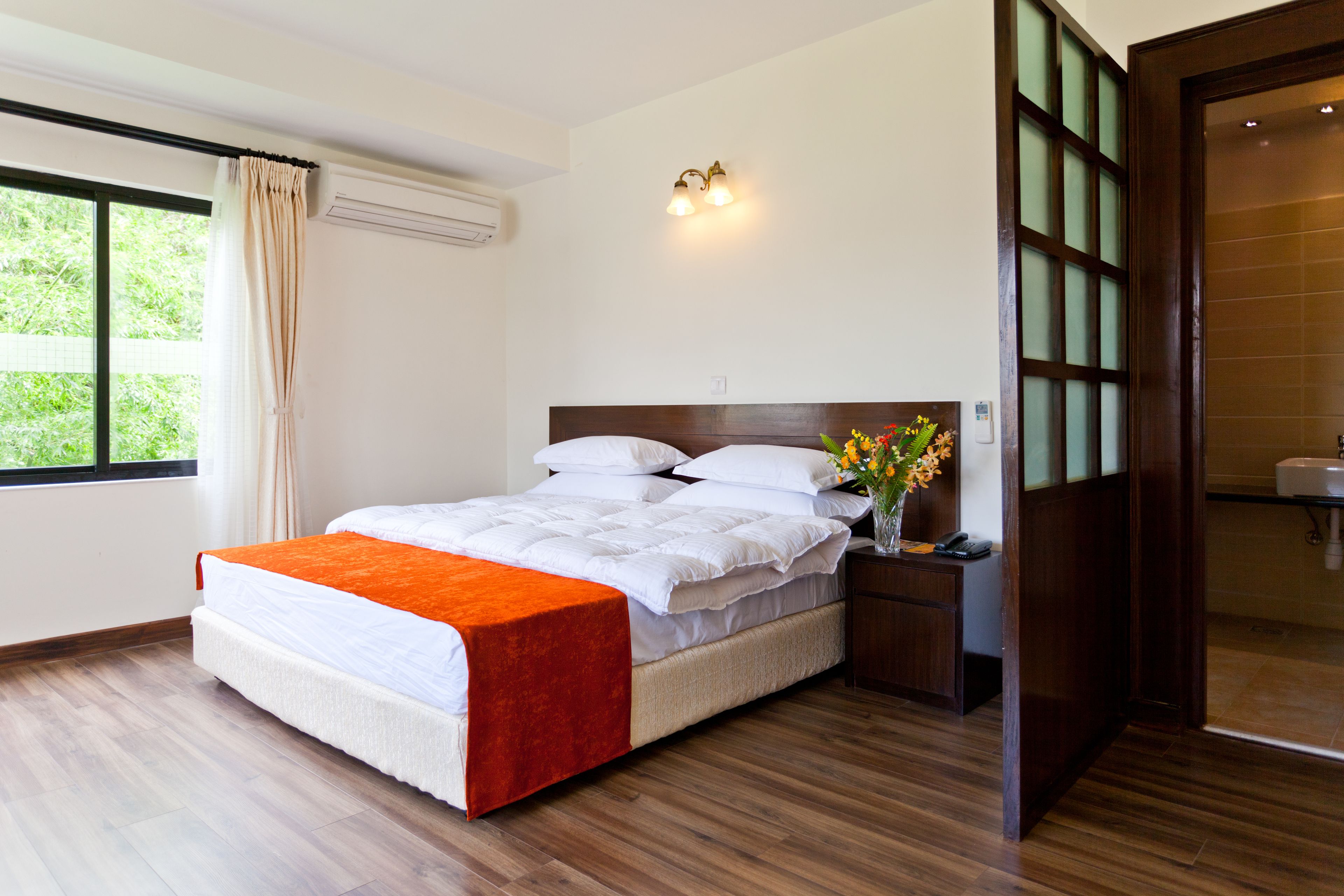 Una cama bien hecha con una colcha blanca y naranja, un cabecero de madera y una mesita de noche con un florero.