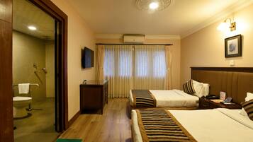 Habitación de hotel con dos camas, piso de madera, baño con inodoro y lavamanos, y un espejo grande.