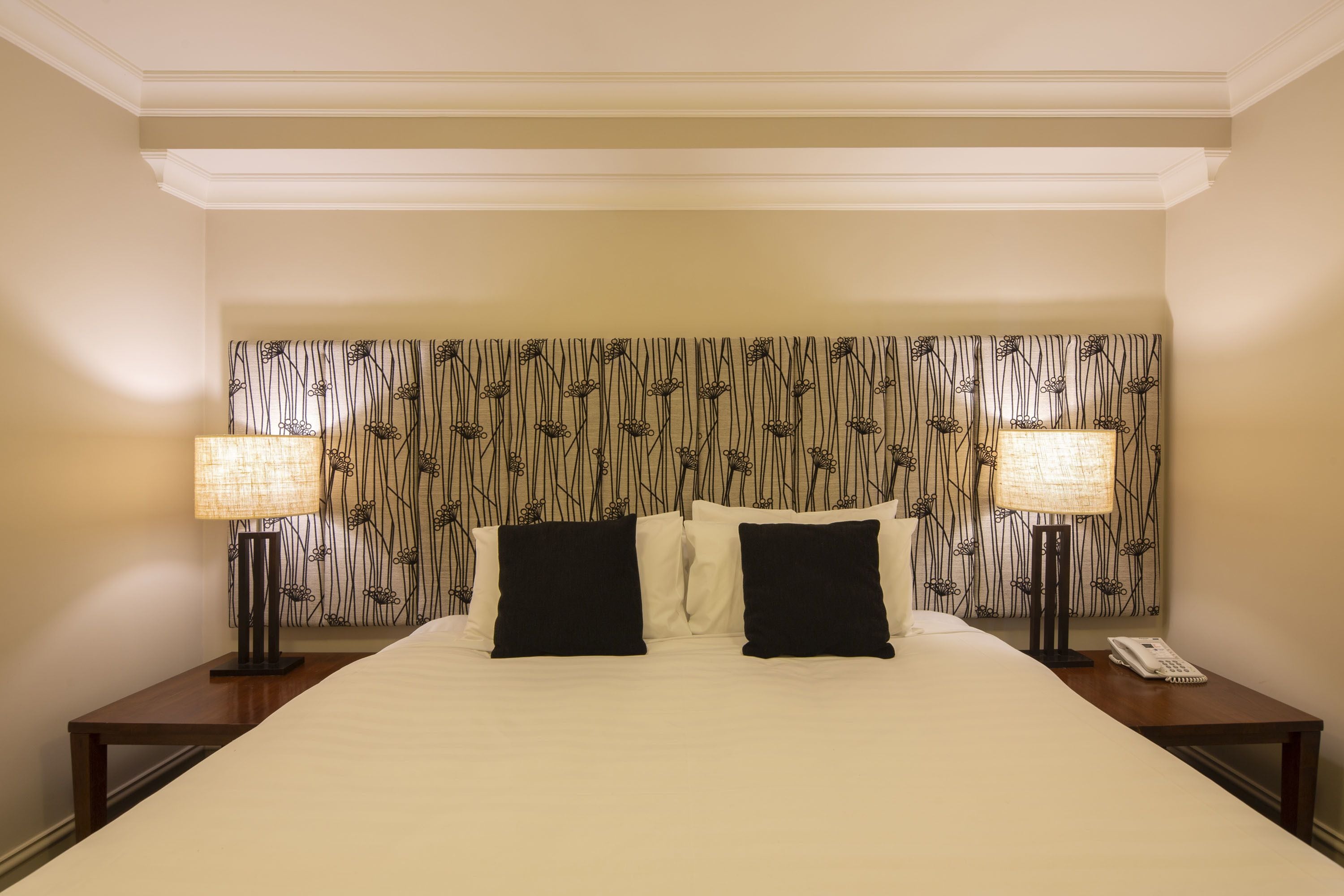 Une chambre d’hôtel avec un grand lit, deux tables de chevet, deux lampes et une tête de lit à motifs.