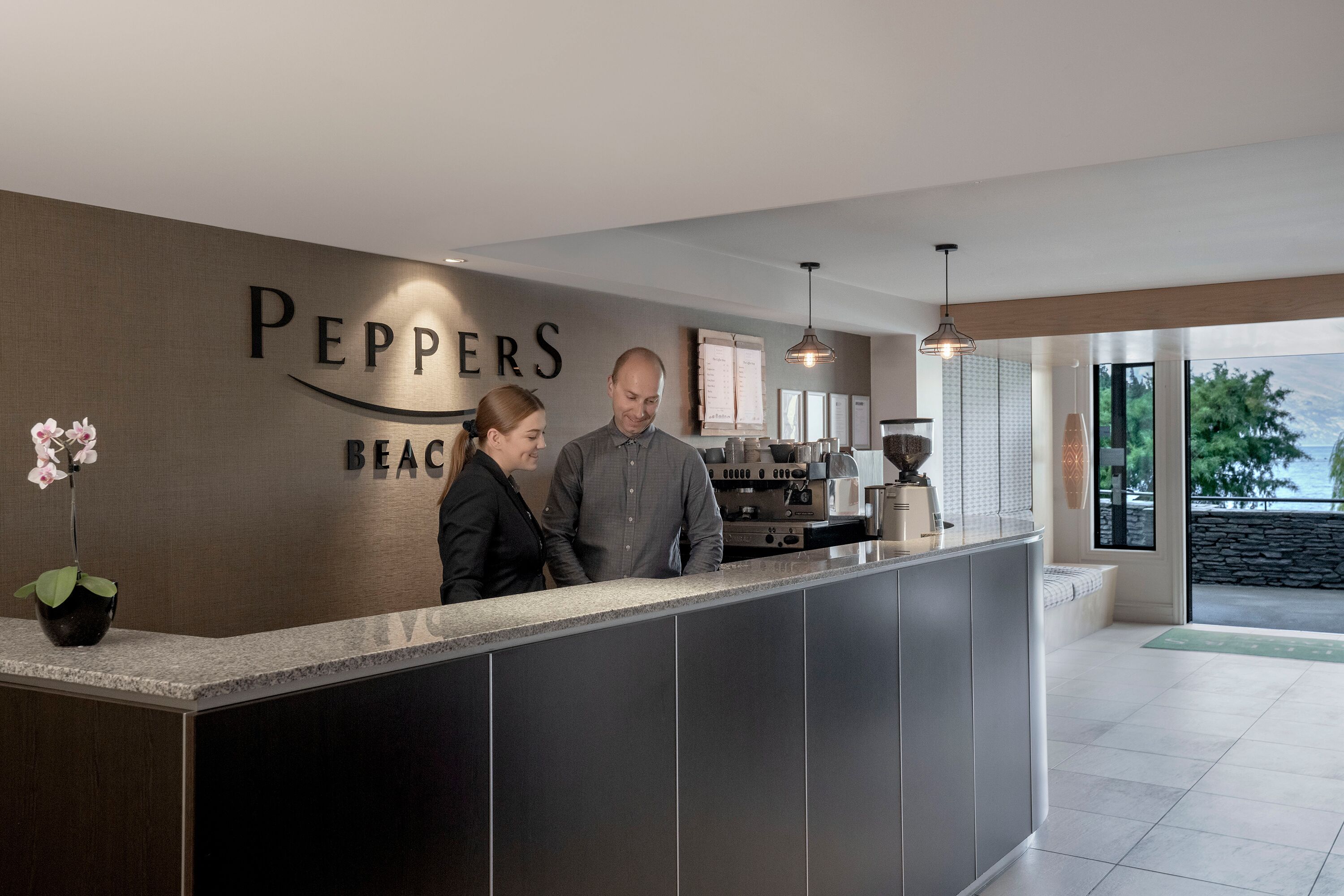 Un comptoir d’accueil avec une enseigne indiquant « PEPPERS BEACH », et un homme et une femme se tenant derrière.