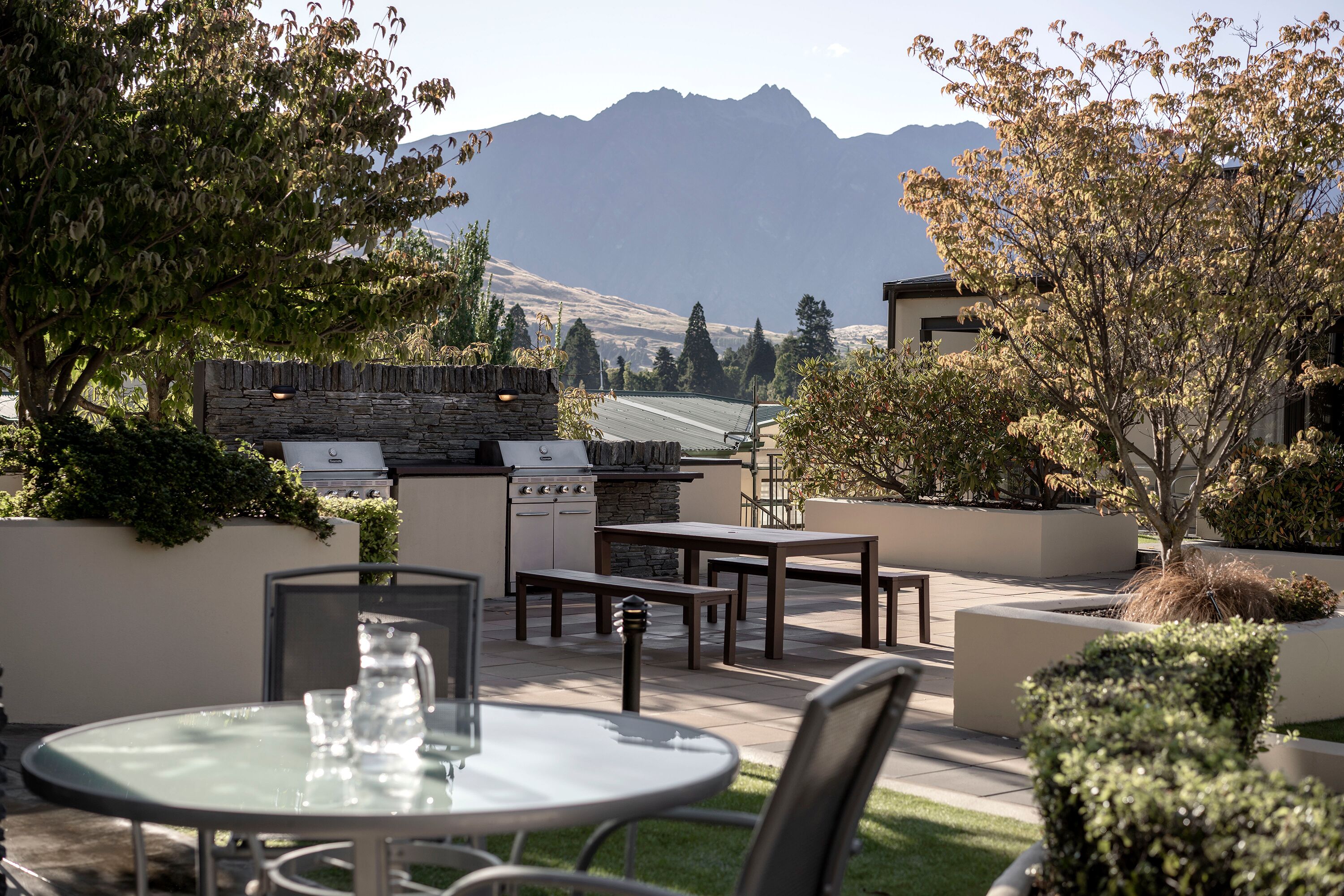 An outdoor patio with a stone wall, a grill, and a table with chairs.