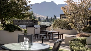 An outdoor patio with a stone wall, a grill, and a table with chairs.