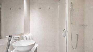 A modern bathroom with a large white sink, a glass shower enclosure, and a mirror.