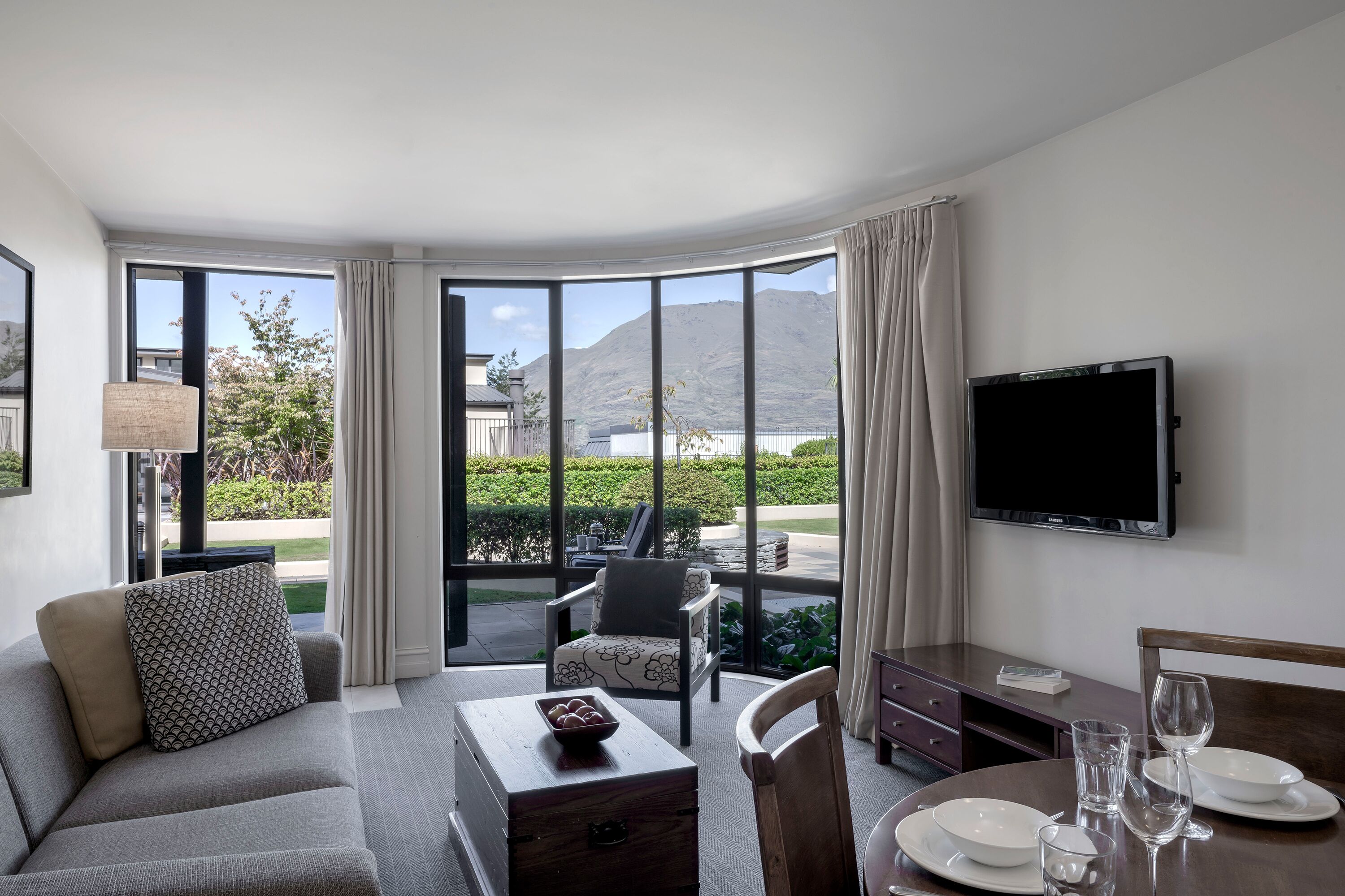 A hotel room with a sofa, armchair, dining table, and a TV.