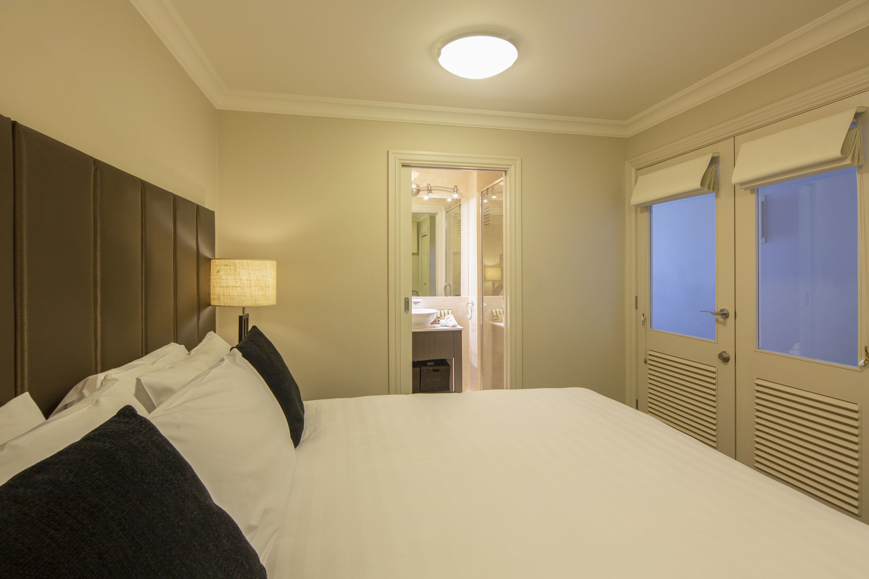 Hotelkamer met een groot bed, een bedlampje, een garderobe met spiegel en een zichtbare badkamer door een open deur.
