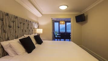 A hotel room with a large bed, a television mounted on the wall, and a view of the outdoors through a door.