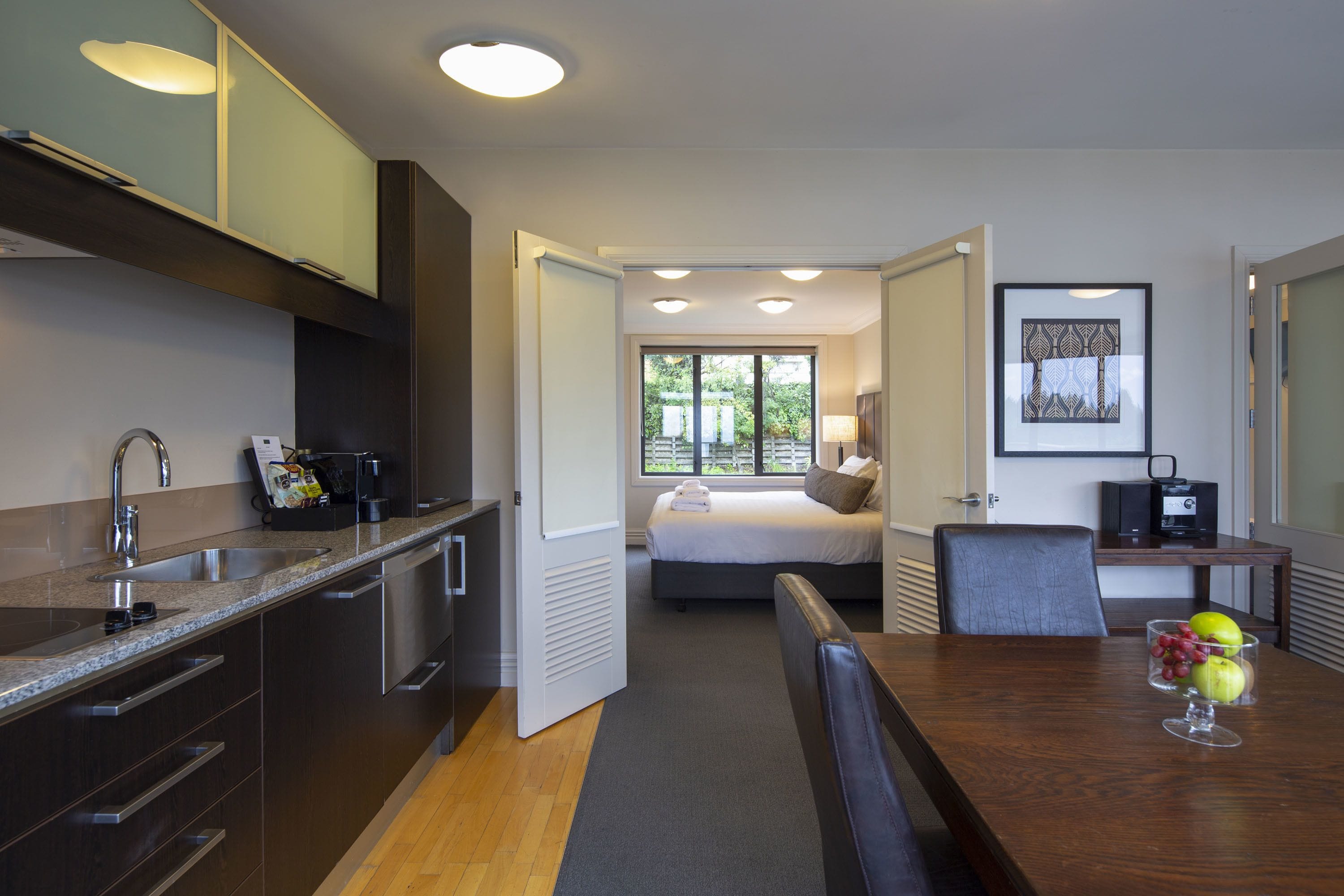 A modern hotel room with a kitchen, a dining area, and a bedroom.