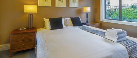 A neatly made bed with white linens and a patterned throw, two bedside tables with lamps, and framed artwork on the wall.