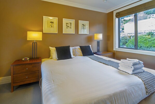 A neatly made bed with white linens and a patterned throw, two bedside tables with lamps, and framed artwork on the wall.