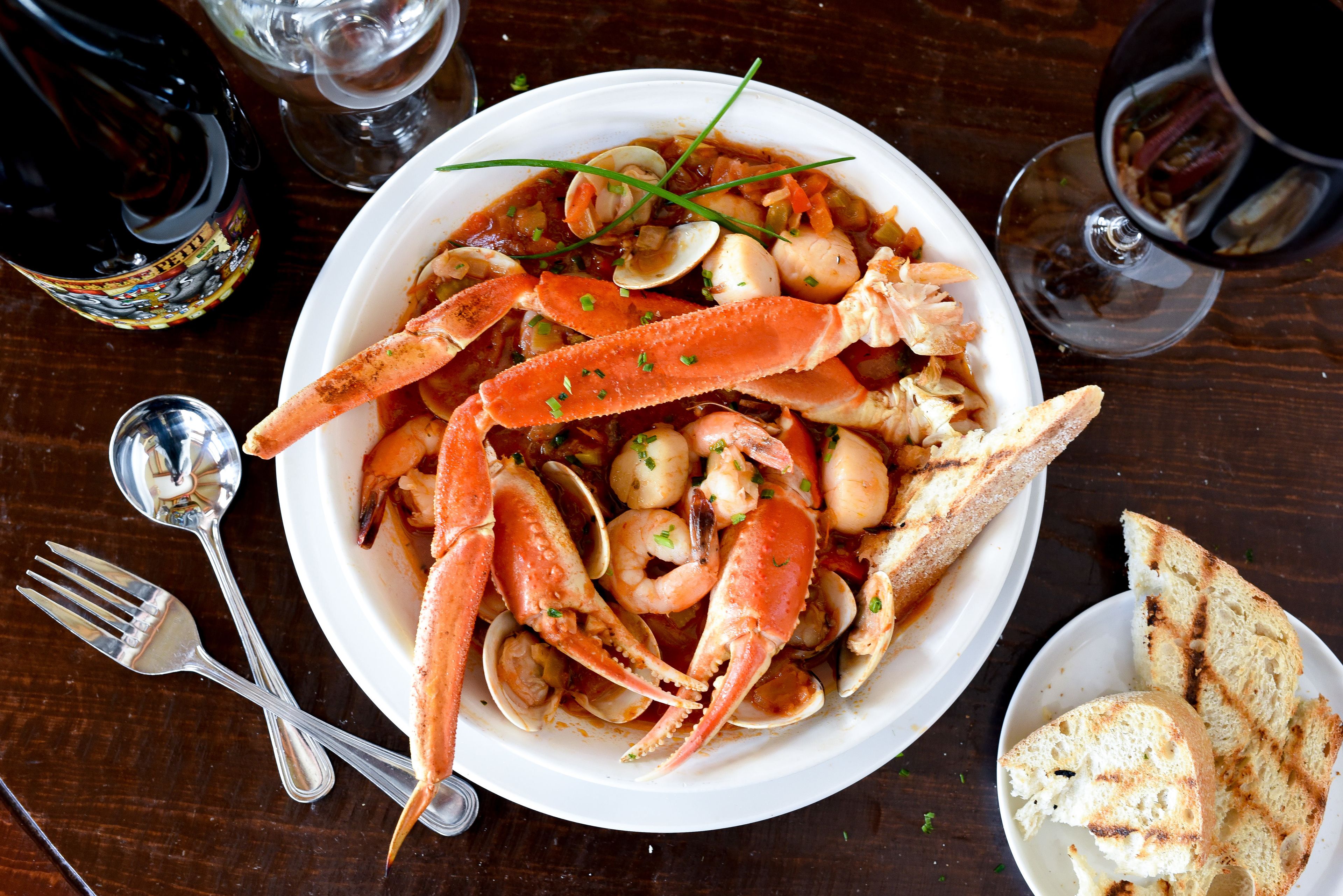 Prato de mariscos com pernas de caranguejo e amêijoas, acompanhado de pão grelhado e uma garrafa de vinho sobre uma mesa de madeira.