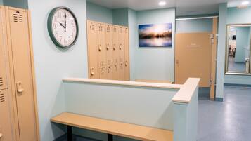 A locker room with beige lockers, a clock, a bench, and a door labeled "Private Baby Changing Station."