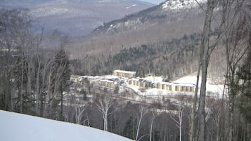 Un paysage enneigé avec un ensemble de bâtiments, probablement un hôtel, entouré d’arbres et avec des montagnes en arrière-plan.