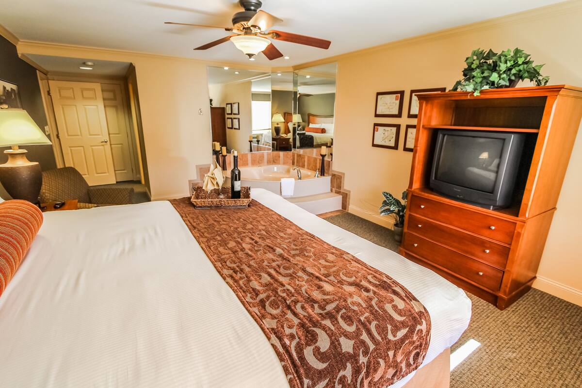 A hotel room with a large bed, a television, a ceiling fan, and a bathroom visible through an open door.