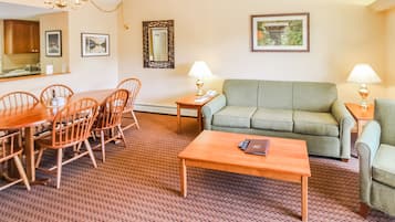 A living room with a green sofa, wooden coffee table, and dining table with chairs. There are two lamps on side tables and a mirror on the wall.