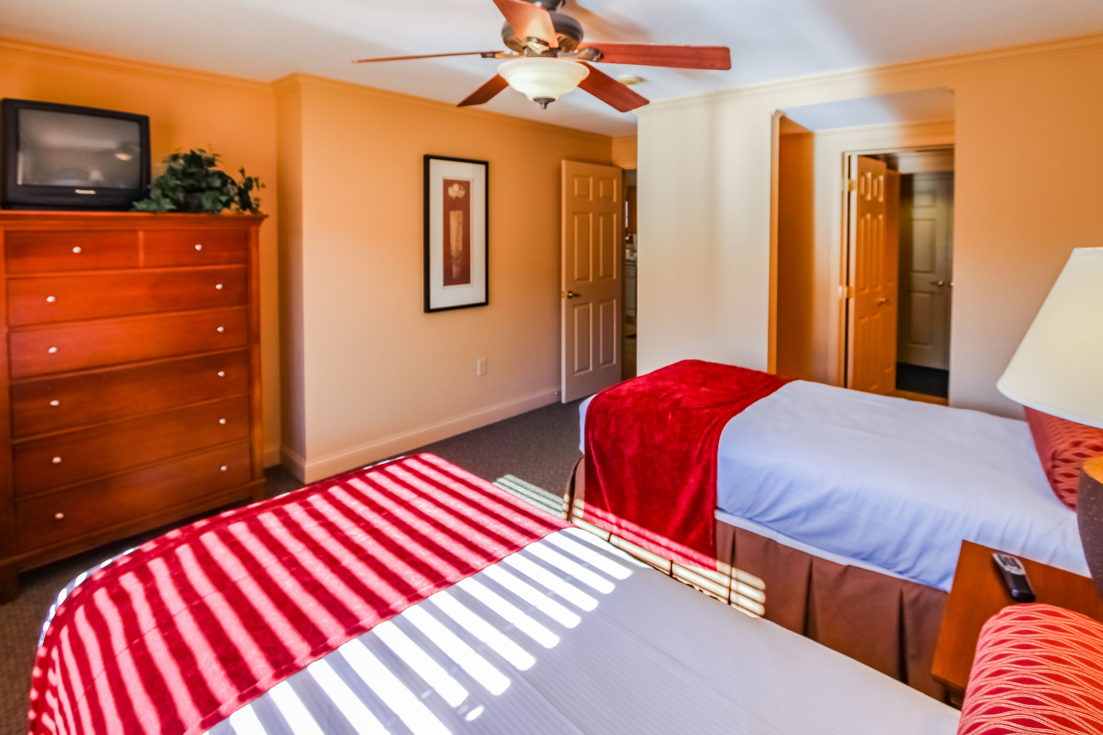 A hotel room with two beds, a wooden dresser, a television, and a ceiling fan.