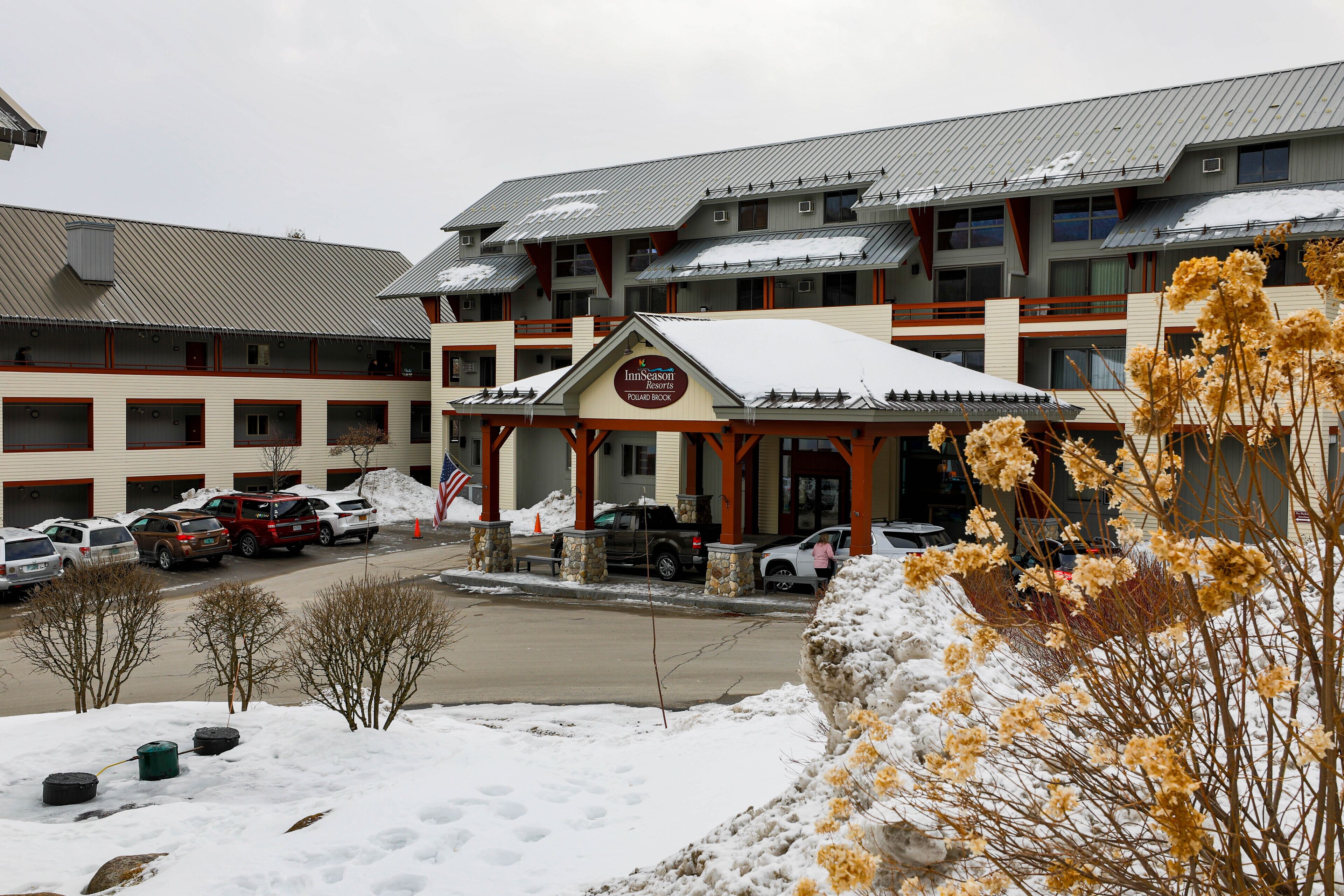 A hotel with a covered entrance, multiple floors, and a parking lot with several cars.