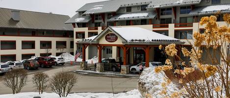 A hotel with a covered entrance, multiple floors, and a parking lot with several cars.