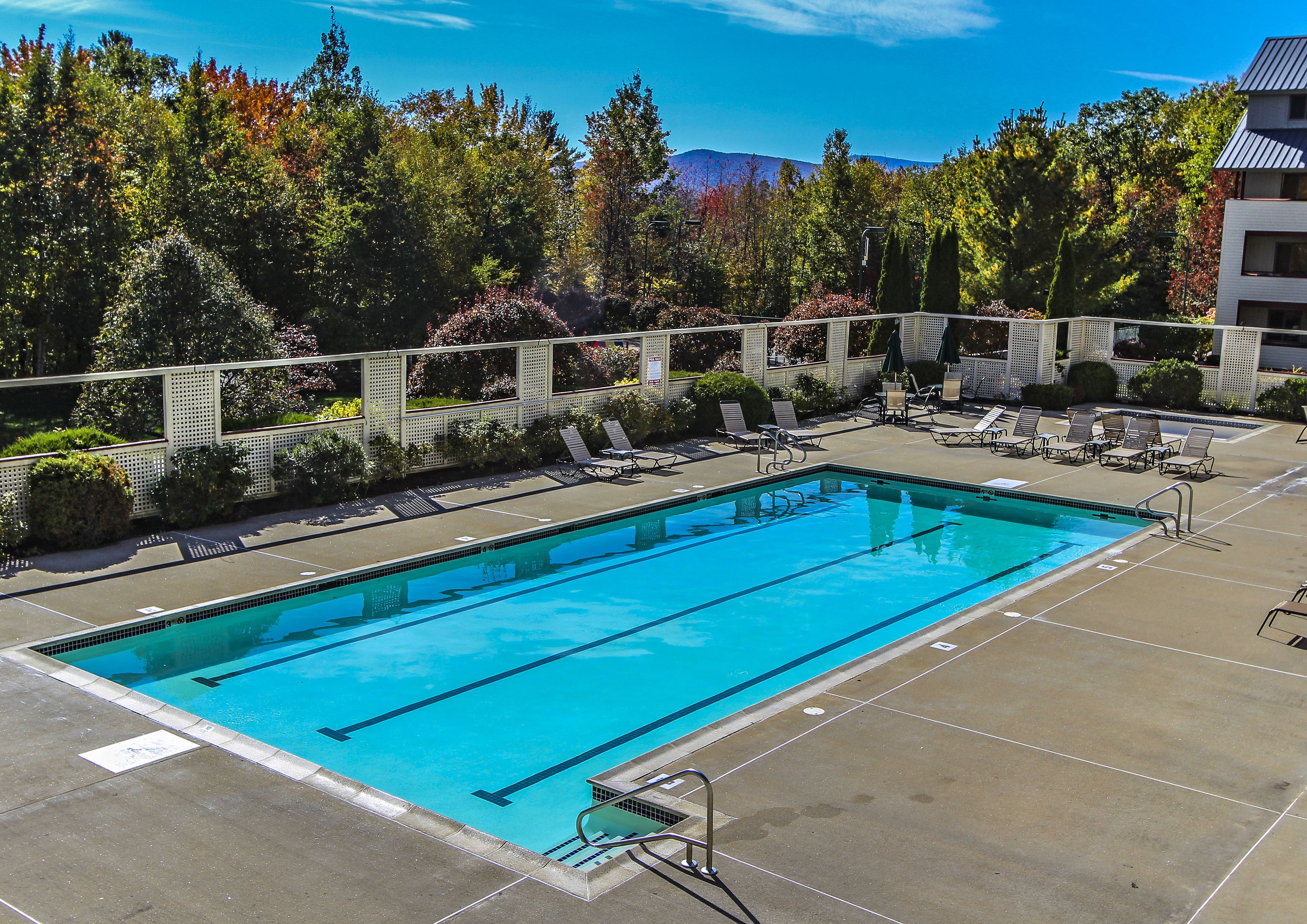 A rectangular swimming pool with clear blue water, surrounded by lounge chairs and a white fence.